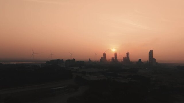 Industrial landscape featuring a cement plant and wind farm under an vibrant orange sky