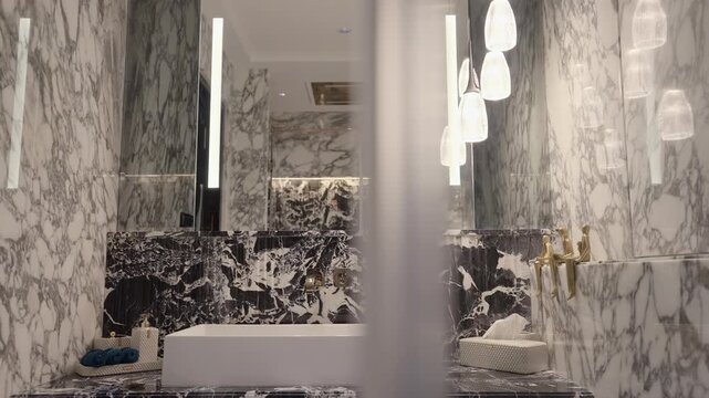 Wide view of sophisticated bathroom with marble walls, rectangular white basin, gold faucets, and hanging glass pendant lights