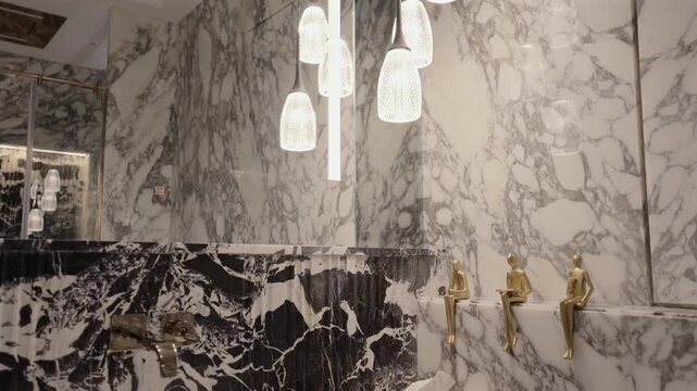 Luxury black and white marble bathroom with gold figurine taps, modern sink, and hanging glass pendant chandelier
