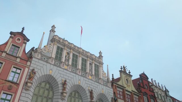 Low angle view of the historic Artus Court and traditional colorful merchant houses in Gdansk, Poland. Ideal for travel documentaries and European heritage content.