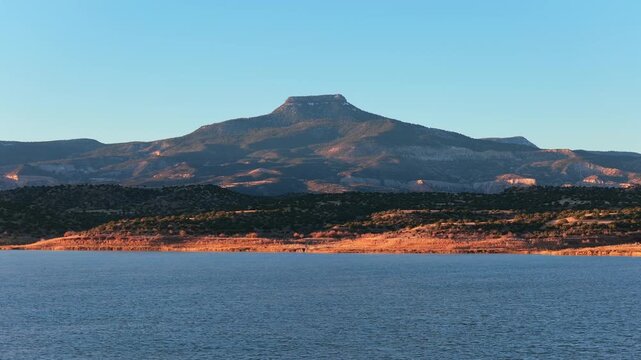 A cinematic drone shot pushing forward toward a flat-top mountain and a blue lake. The camera moves closer to the high-desert peak during warm morning light. Ideal for travel or sci-fi projects.