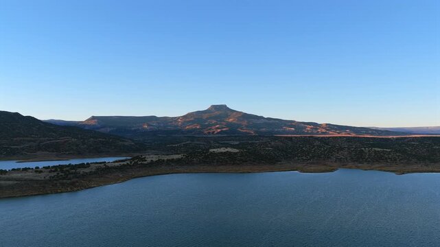 Golden light shines on a flat-top mesa and wide blue lake in Abiquiu, New Mexico. This high-desert scene features long shadows and an epic western horizon, perfect for a cinematic backdrop.
