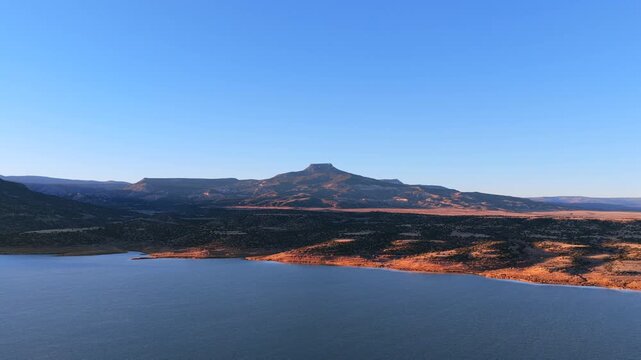 High desert landscape features the volcanic basalt peak of Cerro Pedernal above Abiquiu Lake reservoir. The arid plateau geology of New Mexico offers a stunning background for cinematic travel film.