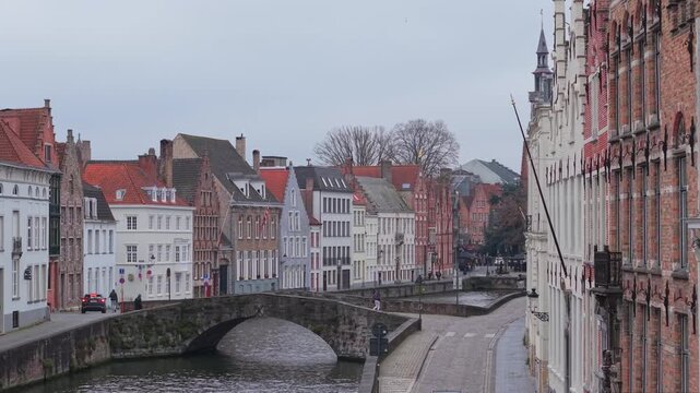Aerial reveal shot over King's Bridge (Koningsbrug) in Bruges, showing traditional waterside houses and the iconic Jan Van Eyck sculpture in the background. Historic Flemish architecture in Belgium.