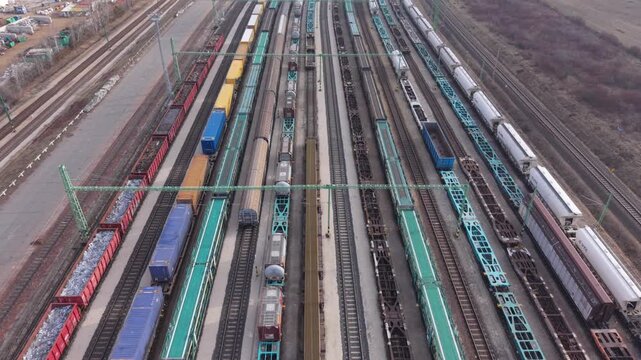 Aerial video of a large railway yard filled with freight trains and cargo wagons aligned on parallel tracks. The video represents modern rail transport, logistics operations, and cargo distribution.