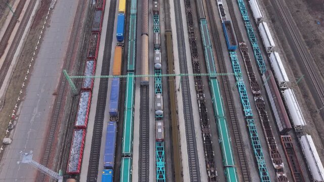 Aerial top view of a large railway yard with multiple freight trains and cargo wagons standing on parallel tracks.
