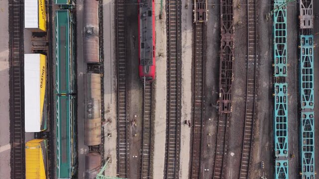 Top-down aerial view of multiple freight trains standing on parallel railway tracks in an industrial rail yard while drone flying over it.