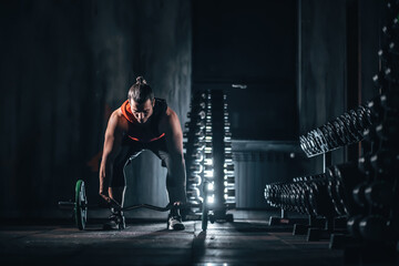 Obraz premium Male bodybuilder preparing barbell deadlift near dumbbell rack in gym, Man training with barbell for strength in fitness gym with dumbbell stand