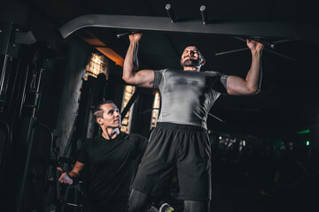 Male bodybuilder performing lat pulldown with personal trainer in gym, Man training back muscles under coach guidance during workout