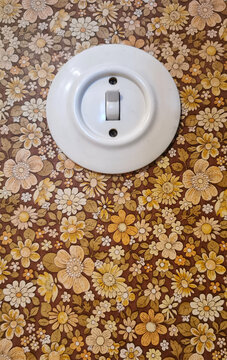 Alter runder Lichtschalter im Innenraum mit Blumenmustertapete