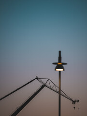 Old crane stands at wharf with lamp post blurred in foreground during early evening in Gothenburg