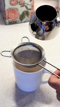 Traditional Pouring Process. Boiled Turkish coffee transferred from metallic cezve through fine strainer into cups on kitchen stove., vertical video, 4k footage