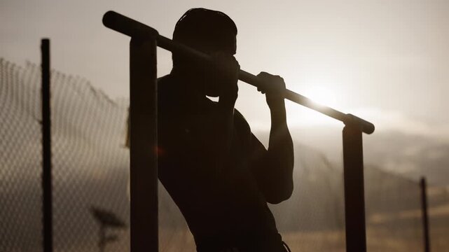 Person doing pull-ups at sunset in an outdoor fitness area with a fence and a clear sky