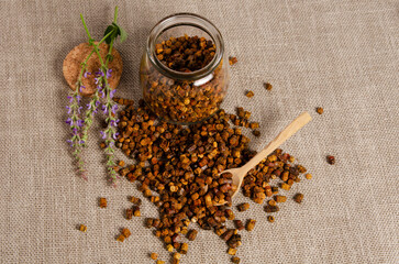 Brown bee bread lies on table in jar with wooden spoon, close-up