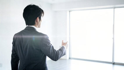 Businessman in suit gesturing towards bright window in modern office