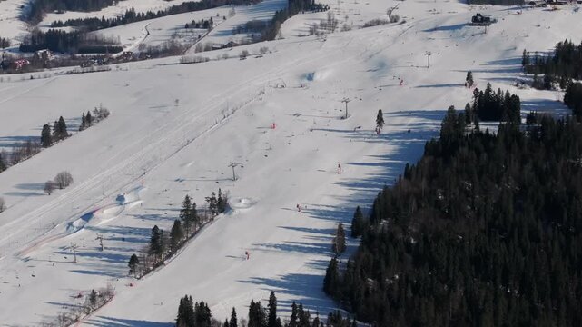 Drone shot of skiers and snowboarders enjoying winter sports on the wide, groomed slopes of Grapa Ski resort with a beautiful mountain backdrop.