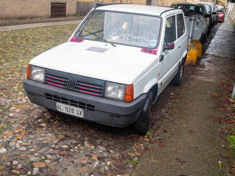 Vintage Fiat Panda parked on a European street with wet cobblestones on a cloudy day, exuding classic urban charm