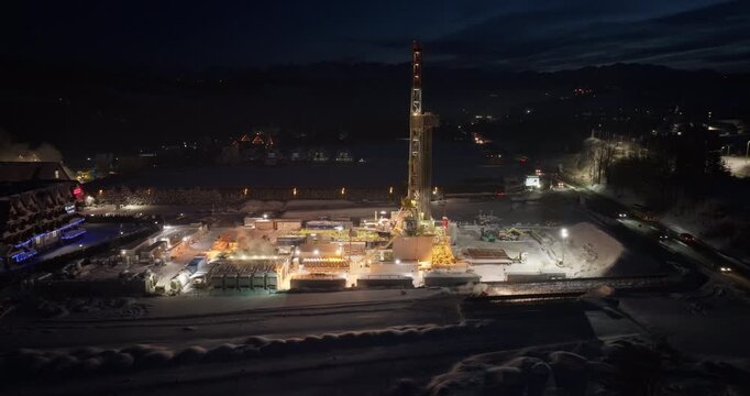 Dynamic aerial tilt-down drone shot showing the complex infrastructure of a geothermal drilling rig in a winter environment.