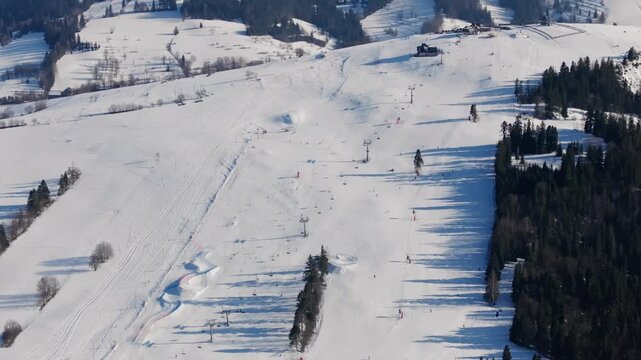 Drone shot of skiers and snowboarders enjoying winter sports on the wide, groomed slopes of Grapa Ski resort with a beautiful mountain backdrop.	
