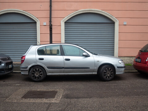Nissan Almera N16 hatchback parked on an urban street alongside other cars, city building background