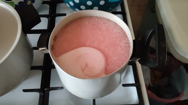 Pink jelly boiling in pot on gas stove