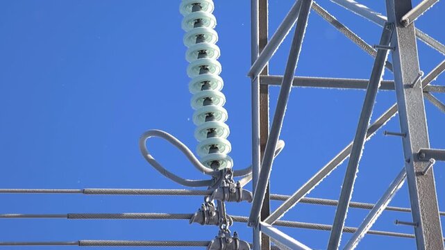 Close view of high voltage suspension insulators coated in ice and hoarfrost on a metal power pylon, sparkling in bright winter sunlight against a deep blue sky.