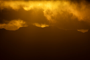 Golden sunset clouds above layered mountain silhouettes © Stoca