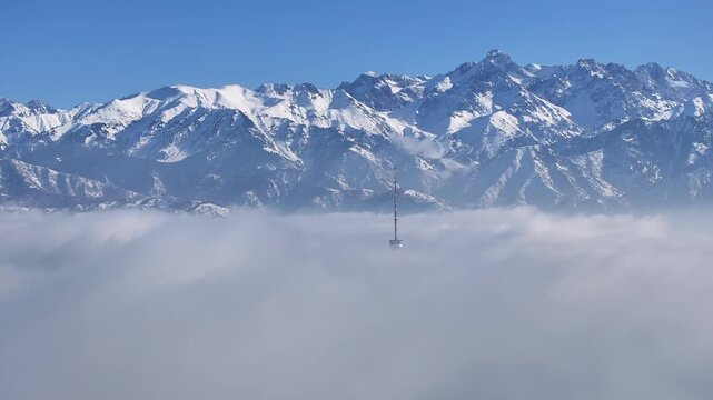 The top of the famous Kok Tobk TV tower in Almaty, Kazakhstan, rises above heavy clouds against the backdrop of the Trans-Ili Alatau mountain range.