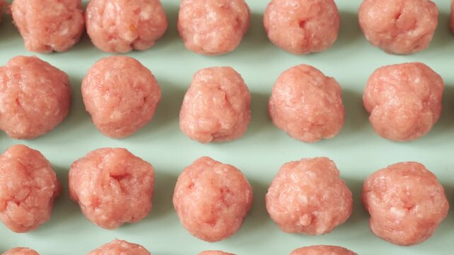 Many raw uncooked meatballs moving in rows on a food production line at a meat processing plant