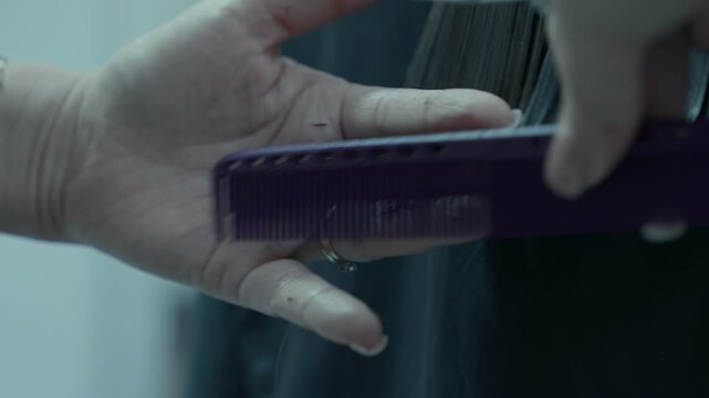 The hairdresser's hands use a comb to straighten the hair and trim the ends.