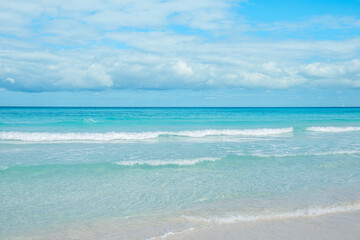 Calm ocean waves gently lap on the sandy shore under a bright blue sky
