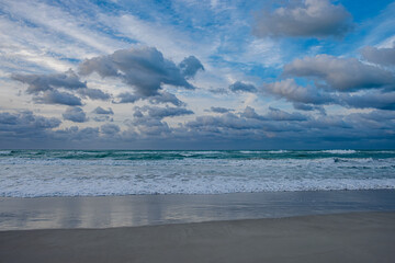 Waves crash on the shore under a cloudy sky at twilight on a beach