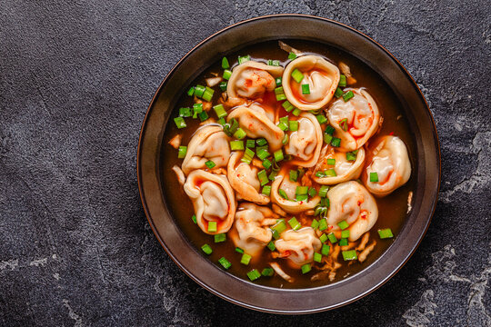 Dumplings served in a bowl with broth and green onions.