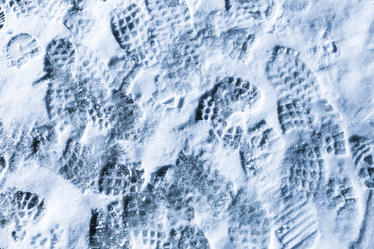 Overlapping shoe prints in fresh snow surface. Winter ground texture with many boot footprints. Cold weather background showing human activity outdoors. Trampled snowy path detail.