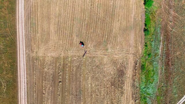 Static overhead drone shot of a red tractor raking hay for bales in a cultivated field, emphasizing agricultural patterns, machinery movement, and rural symmetry.