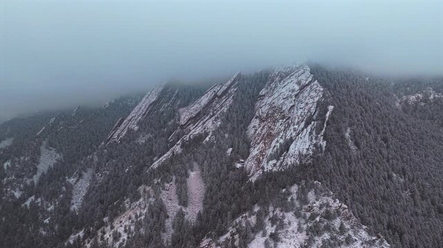 Winter lightly snowing Flat Irons rock formations slabs Chautauqua Park trail Boulder Colorado aerial drone sunset dusk evening snowy trees snow falling foggy grey skies low cloud layer forward motion