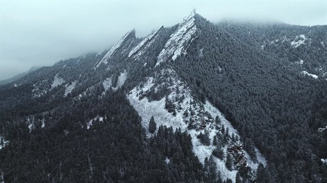 Winter snowing fog Flat Irons rock formations slabs Chautauqua Park trail aerial drone Boulder Colorado sunset dusk evening snowy trees snow falling foggy grey skies low cloud layer forward pan up