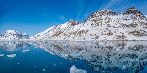 Spitzbergen, Svalbard, Norwegen: Arktische Gebirgslandschaft spiegelt sich im stillen Wasser des Magdalenefjorden mit Treibeis unter strahlend blauem Himmel. © stylefoto24