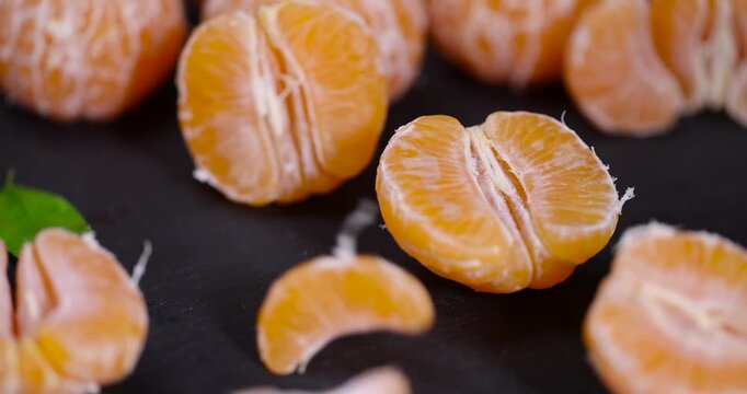 sliced juicy peeled orange tangerine on a black slate table, ripe orange mandarin without peel on a black slate board, tangerine divided into small slices
