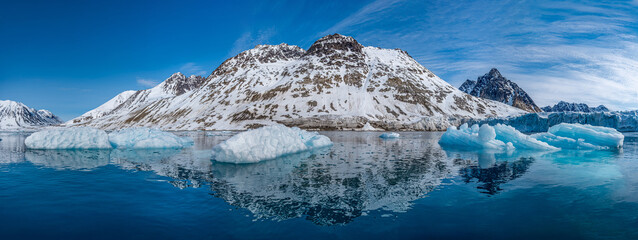 Spitzbergen, Svalbard, Norwegen: Arktische Gebirgslandschaft spiegelt sich im stillen Wasser des Magdalenefjorden mit Treibeis unter strahlend blauem Himmel. © stylefoto24