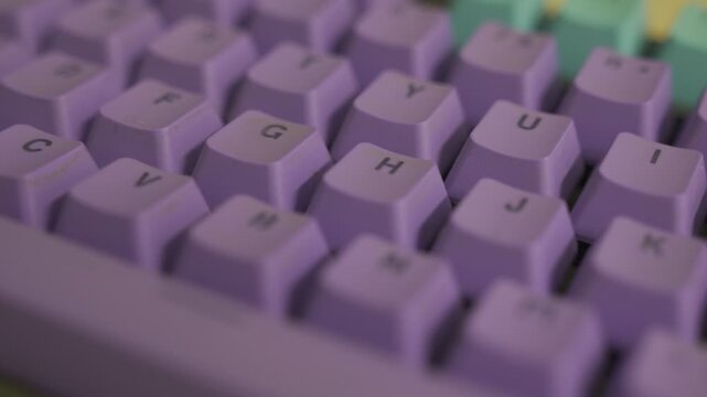 Close-up of purple mechanical keyboard keys. Focus shifts across the keyboard. The keys display letters. Lighting is soft and diffused. Shallow depth of field