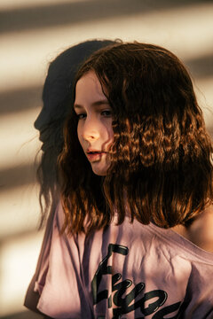Girl with Wavy Brown Hair in Sunlight with Shadow on Wall.