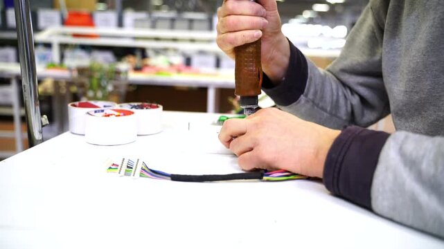 Close-up of a blue-collar worker using an electric screwdriver to assemble cable terminals in a small workshop. Concept of small business manufacturing, manual labor, and electrical craftsmanship.