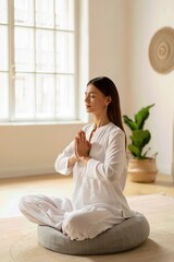 Woman sitting in peaceful home practicing meditation on yoga cushion, finding balance, relaxation, and wellness with eyes closed and hands in namaste mudra.