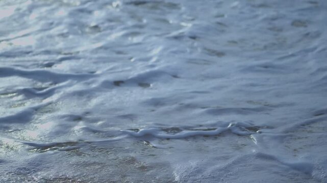 Ocean wave washing over sandy beach with white sea foam. Calm atmospheric seascape showing movement of water, natural texture, and peaceful coastal mood.