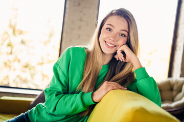 Naklejka premium Portrait of a young woman enjoying leisure time in a modern home, wearing a green sweatshirt and displaying a cheerful smile