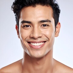 Young man with dark hair smiles broadly, showing teeth against a plain background, chest and shoulders visible