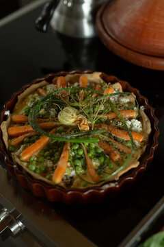 Homemade Savory Vegetable Tart with Carrots, Peas, and Fresh Herbs in a Rustic Ceramic Dish
