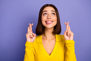 Happy young woman in yellow top crosses fingers and smiles against purple background for lifestyle...