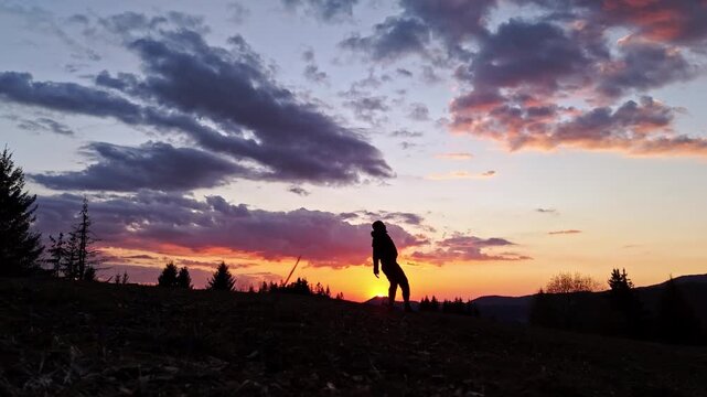 Silhouette of a person doing a cartwheel on a mountain hill during a dramatic sunset.